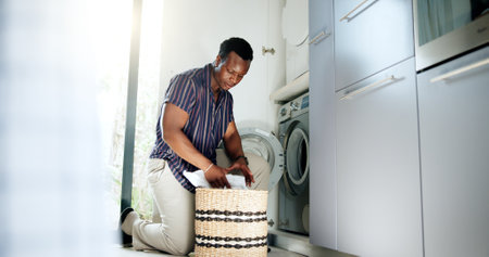 Laundry, black man and clothes basket with washing machine, housekeeping and cleaning routine for fresh linen. Hygiene, person and fabric in appliance for domestic chores and housework in washroomの写真素材