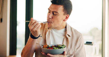 Nutrition, eating and man with salad in kitchen in home for organic vegetable bowl. Vegan, health and male person enjoying fresh produce for snack or lunch on diet, vitamins or wellness in house.の写真素材