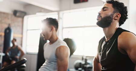 Exercise bike, fitness and tired with men in gym together for break from cardio training or workout. Breathing, elliptical machine and sweating with sporty friends in health club for workout togetherの写真素材