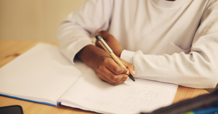 Hands, writing and child with notebook, desk and education for student, growth and development in school. Table, pupil and kid with assessment, closeup and youth with scholarship in classroomの写真素材