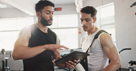 Fitness, advice and men in gym with tablet for online registration, planning or workout schedule. Athlete, personal trainer and digital app for exercise, progress results or membership at sports clubの写真素材
