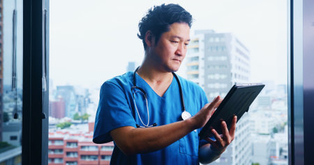 Japanese, man and surgeon with tablet for test results, medical research or appointment booking. City, window or doctor with touchscreen for online browsing, schedule or health app at hospital clinicの写真素材
