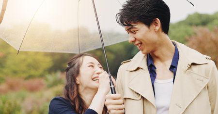 Love, umbrella and laughing with Japanese couple in park for romance, bonding and relationship. Support, funny and happiness with man and woman in Japan nature for date, commitment and peaceの写真素材