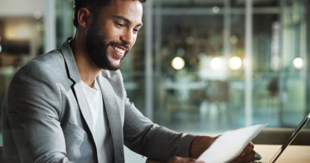 Laptop, auditor and businessman reading paperwork for profit report, bookkeeping or revenue at night. Computer, document and happy accountant check information, finance results or savings on overtimeの写真素材