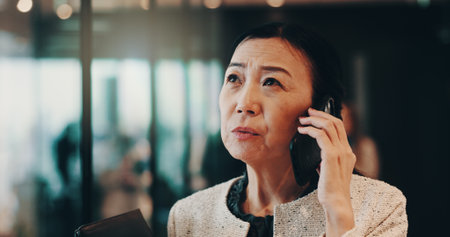 Japanese, woman and office with phone call for communication, court ideas and networking with contact. Female person, mature lawyer and thinking with client for negotiation, business and mobile chatの写真素材