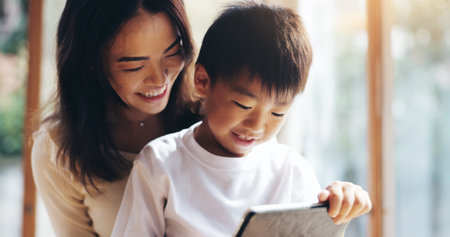 Mother, son and tablet in home for bonding, playing games or streaming cartoon video with internet. Japanese family, boy and mom together with technology for teaching, development or online educationの写真素材