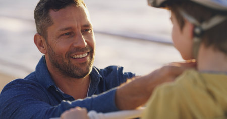 Happy dad, child and helmet with help for protection, learning or teaching son to ride a bike in neighborhood. Parent, kid or boy with safety for cycling, bicycle lesson or practice at outdoor parkの写真素材