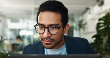 Glasses, laptop and online with business man in office for journalist, article proofreading and editor. Email, news and report with employee in startup agency for reading, network and projectの写真素材