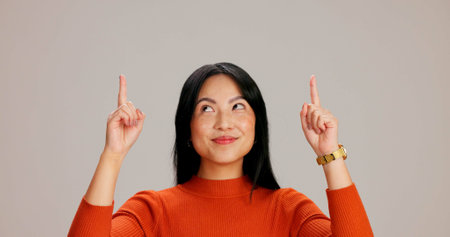 Asian woman, point up and smile with choice, promotion and deal with mock up space by background. Japanese girl, person and model with direction, decision and show with sign, emoji or announcementの写真素材