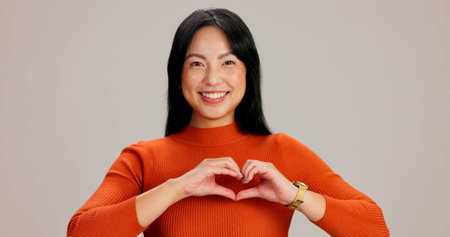 Asian girl, heart hands and happy in studio portrait, excited and icon with kindness, care and love by background. Woman, person and model with symbol, emoji and sign for valentines day in Taiwanの写真素材