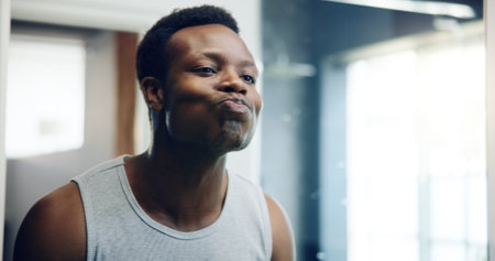 African man, bathroom mirror and check for skin with results, reflection and shaving with grooming in home. Person, glow and facial change in morning with thinking, hygiene and cosmetics at apartmentの写真素材
