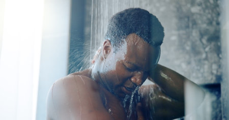 Black man, shower and splash in home, bathroom and washing body for hygiene with self care in morning. Person, water and cleaning for skin, routine and bacteria with grooming process at apartmentの写真素材