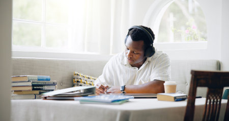 African man, student and headphones in home with books, writing or learning with listening to music with scholarship. Person, notes and streaming with studying, education or planning for college examの写真素材