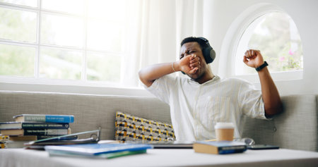 Black man, student and tired with yawn in home with headphones, books or learning with music for...