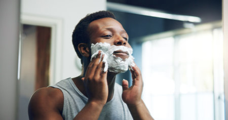 Black man, shave and mirror with face cream for grooming, epilation or hair removal in bathroom at home. African, male person or facial with aftershave creme for clean beard or skincare routineの写真素材