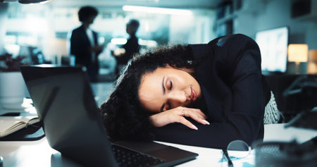 Night, woman or sleeping in office with fatigue, burnout or tired at business laptop. Accountant, tech and resting on desk in overtime, missed deadline or mental health risk with low energy in agencyの写真素材
