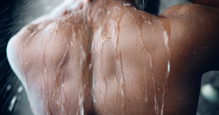 Man, back and water in bathroom for shower, washing and hygiene in morning routine for care. Person, wet splash and cleaning in home for grooming, skincare and skin hydration with relax for wellnessの写真素材