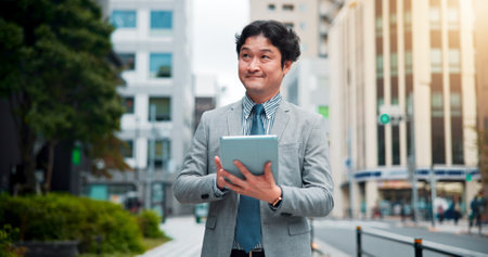 Japanese man, city street and tablet for location search, direction and navigation with happiness. Male person, technology and smile on sidewalk for commute, travel and walk as real estate developerの写真素材