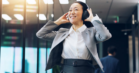 Woman, headphones and employee walking in office, hearing music and celebration of success. Female person, professional and morning dancing in workplace for achievement, listening and sound in Japanの写真素材