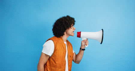 Man, profile and protest with megaphone in studio for strike, announcement or message on a blue background. Male person, rebel or march with loudspeaker or bullhorn for awareness or alert on spaceの写真素材