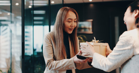 Business people, gift and celebration with bow, gratitude and congratulations. Japan, employees or consultant in office, present and event for birthday, success or promotion with respect or thank youの写真素材