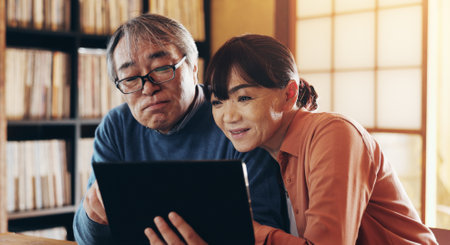 Love, retirement and tablet with senior couple in home together for browsing or social media. App, internet or technology with old Japanese man and woman in apartment for online travel bookingの写真素材