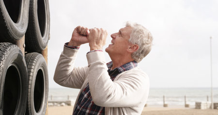 Happy, senior man with fist at beach playground for cheering, equipment and adventure success. Smile, grandfather and support child for climbing games, balance safety and bonding together of activityの写真素材