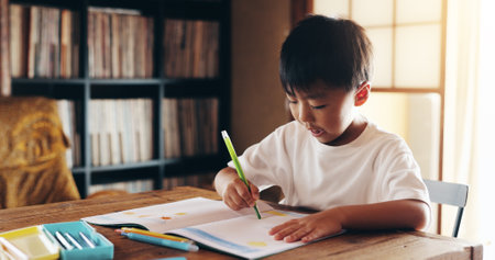 Asian boy, writing and learning with book for drawing, sketching or childhood development at home. Japan, kid or child with coloring crayons, talent or skill for creativity, art or education at houseの写真素材