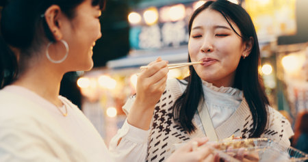City, asian women and happy with street food, travel and snack for friends with meal, students and road. Outdoor, delicious and cuisine for celebration of reunion, people and sharing in Japanの写真素材