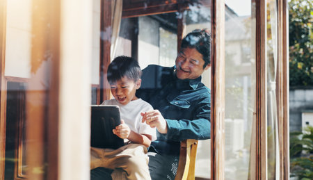 Father, son and tablet in home for bonding, playing games or streaming cartoon video with internet. Japanese family, boy and dad together with technology for teaching, development or online educationの写真素材