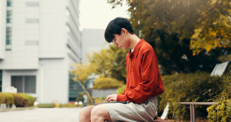 Man, student and laptop in city with typing, planning and creative writing for travel blog in Japan. Japanese person, computer and outdoor in Tokyo with social media post, journal editing and emailの写真素材