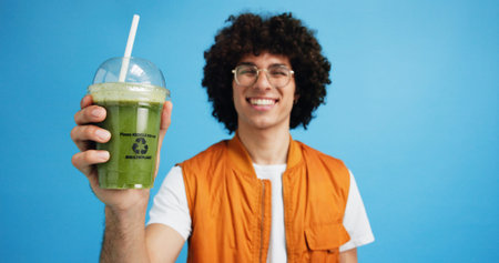 Drink, man and portrait with smoothie in studio, digestive health and fruit juice in recycled plastic. Mockup space, nutritionist or smile with container for green shake, nutrition or blue backgroundの写真素材