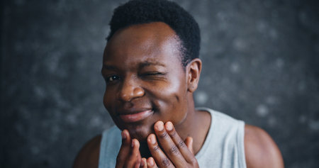 African man, skincare and portrait with check for results, glow and change with smile in morning. Person, happy and wink with cosmetics, wellness and facial transformation at apartment in Nigeriaの写真素材