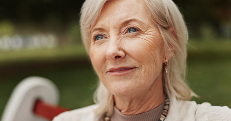 Mature woman, thinking and outdoor in park for memory, reflection and nostalgia with happiness. Female person, smile and relax on break or rest in nature for calm, environment or fresh air on weekendの写真素材
