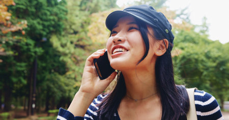 Happy, asian woman and nature with phone call for travel, sightseeing or communication at park. Japan, female person or tourist with smile on mobile smartphone for conversation, destination or chatの写真素材