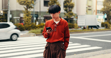 Reading, phone and Asian man in city for social media, online text and internet in street. Travel, networking and person on smartphone for website, digital map and navigation on weekend in Japanの写真素材