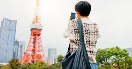 Holiday, photography and person with smartphone, city and capture of landmark, screen and content creation. Outdoor, influencer and tourist with mobile, display and picture of Tokyo Tower in Japanの写真素材
