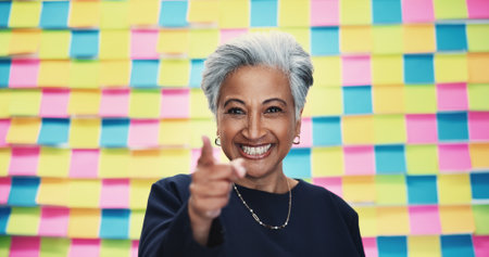 Mature, portrait and happy woman pointing with colorful background for selection, choice or pick in studio. Female person, CEO or creative with smile or finger gesture to you for decision or optionの写真素材
