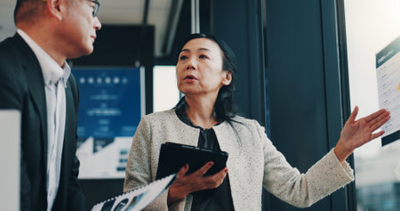 Asian, business people and presentation with tablet for company policy, schedule or planning at office. Japan, businessman and woman with documents or technology for corporate proposal at workplaceの写真素材