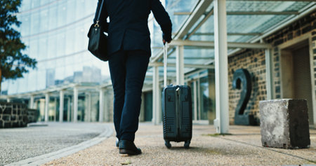 Legs, business and travel with luggage in city for journey, corporate trip or immigration flight at airport. Suitcase, back or person walking to building, hotel or passenger commute outdoor on streetの写真素材