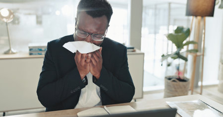 Sick, black man and blowing nose with tissue for viral infection, hayfever or allergies at ofice. African, businessman or employee with virus, cold or flu for influenza, cough or sneeze at workplaceの写真素材