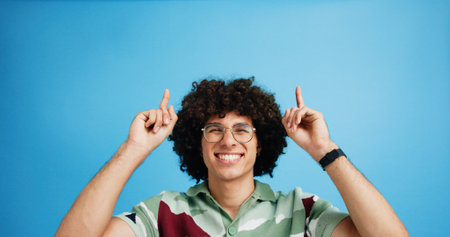 Pointing up, portrait and man with opinion, announcement and advertising smile in studio. Blue background, brand promotion and person with hand gesture, confidence and information in mockup spaceの写真素材
