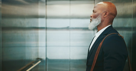 Business, man and travel in office elevator for morning commute, journey to work or waiting to exit. Mature professional, black employee and bag in lift for leaving building, company floor or arrivalの写真素材