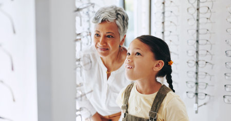 Child, optometrist and choosing frame at store, prescription glasses and helping client. Woman, optical clinic and specialist consulting on lens for girl, kid appointment and service at eye examの写真素材