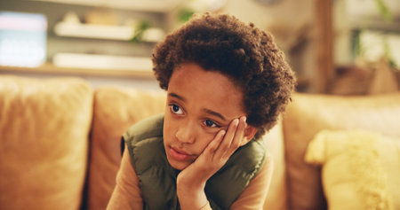 Stress, sad and bored child on sofa with mental health, fatigue and frustrated loneliness in home. Anxiety, thinking and tired African boy kid with depression, memory and emotional burnout in growthの写真素材
