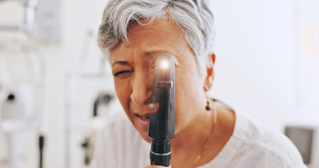 Eye exam, light and retinoscope with mature woman in clinic for optometrist, healthcare and vision. Medical, ophthalmologist and glaucoma test with person and tools for retina, pov and assessmentの写真素材