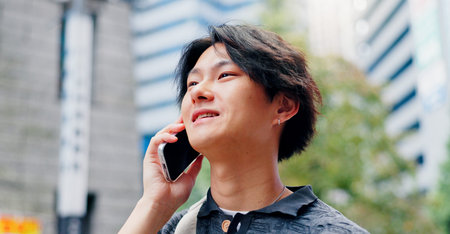 Japanese man, talking and phone call for communication, discussion and booking with travel in city. Person, happy and mobile outdoor for listening, conversation and morning commute with chat.の写真素材