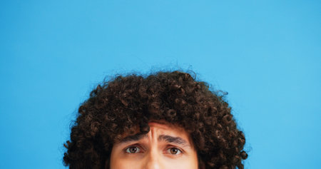 Raised eyebrow, confused or man in studio portrait with puzzled expression, emoji or eyes. Curly, unsure or afro hair guy with doubt, question or worry on blue background mockup for styling productの写真素材
