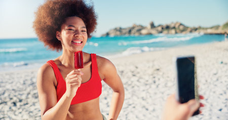 Phone, photography and woman on beach with smile, friends and frozen dessert on fun summer vacation. Smartphone, holiday and happy people at ocean with digital memory of outdoor travel adventureの写真素材