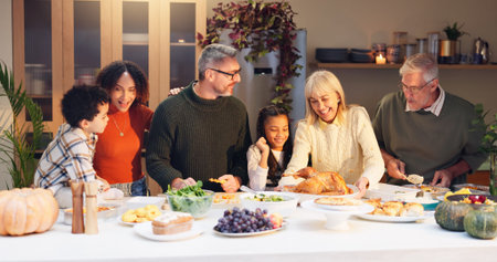 Happy family, serving chicken and thanksgiving with children, event and food for holiday or vacation. Feast, people and interracial parents at dinner party, reunion and gathering for bonding in homeの写真素材